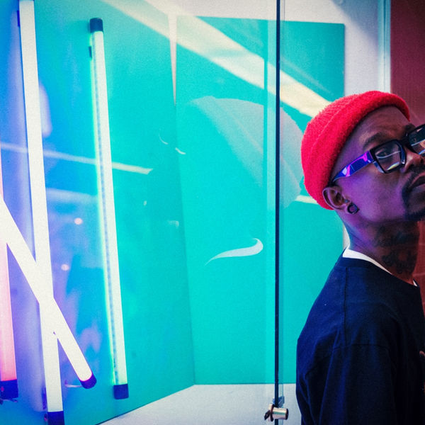 Model in a red beanie beside teal neon tubes